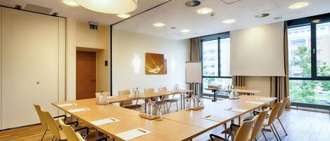 A conference room with a long table, chairs, a whiteboard, and a large window with a view of buildings.