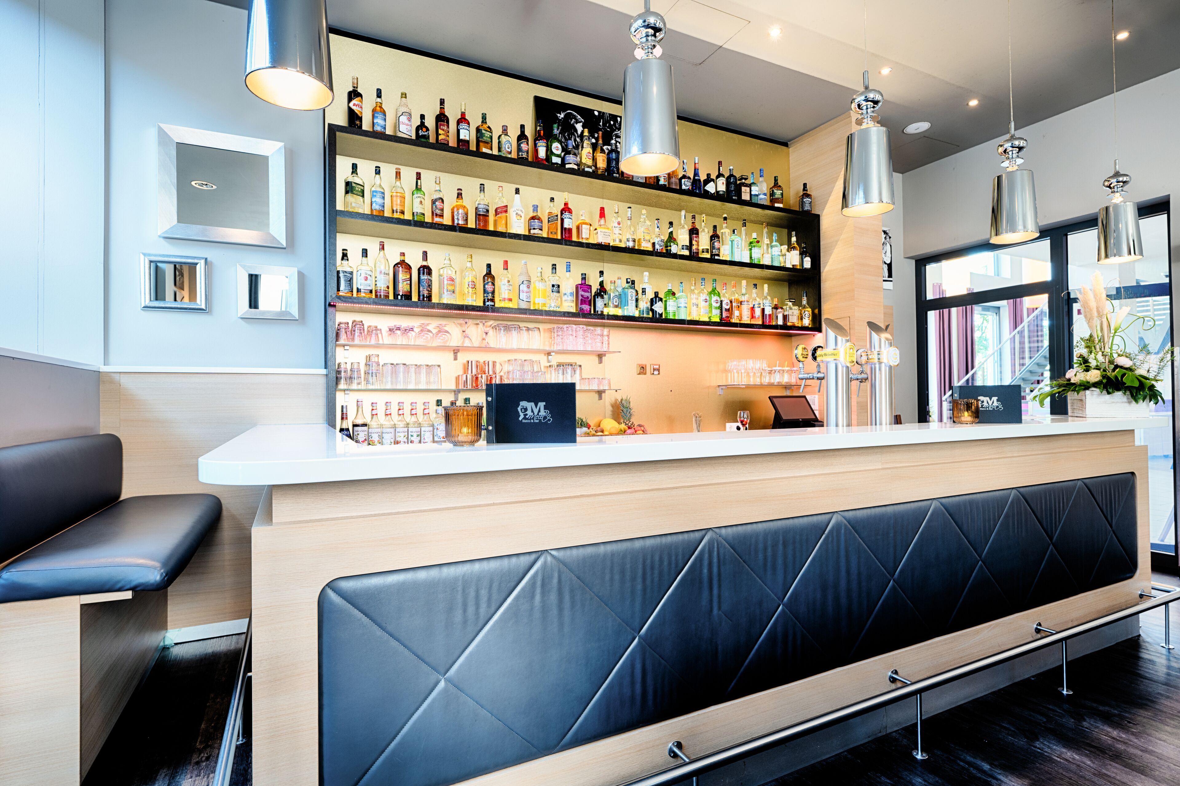Een bar met flessen drank, een toonbank en zitplaatsen.