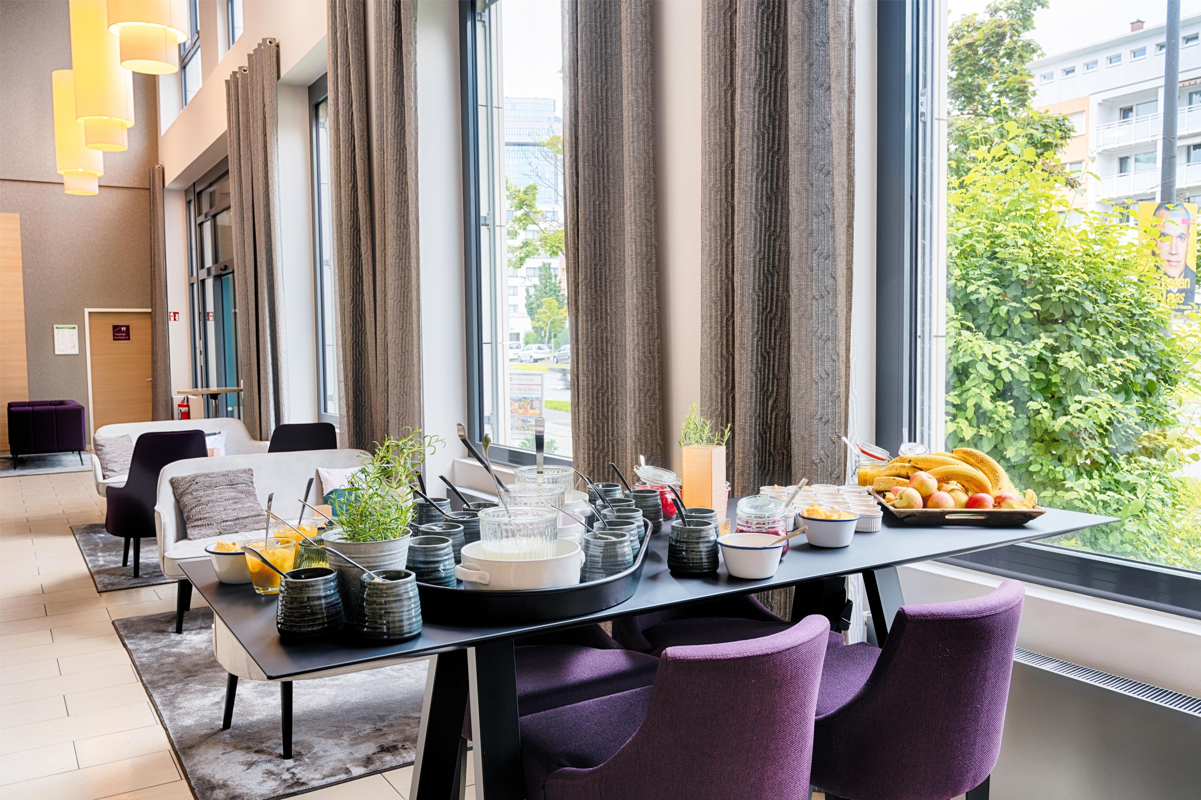 A modern dining area with a table set for breakfast, featuring various food items and utensils.