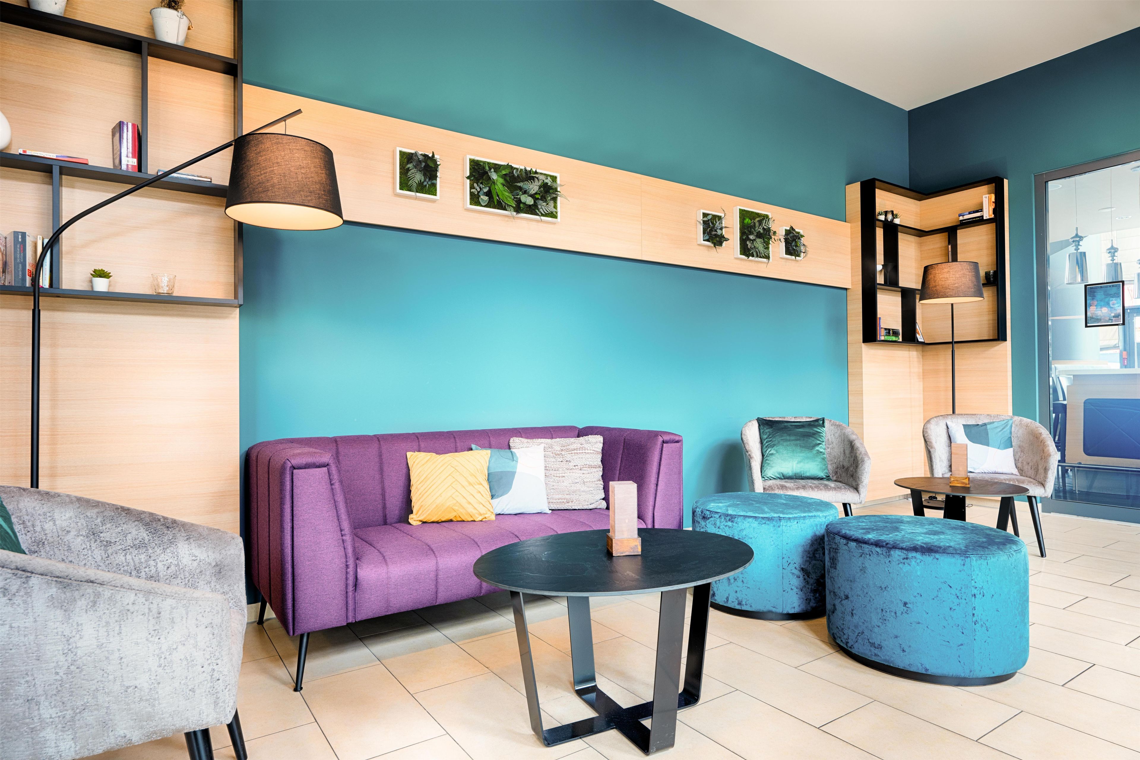 Ein modernes Interieur mit einem violetten Sofa, runden blauen Hocker, einem schwarzen Tisch und einer Deckenleuchte.