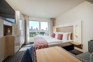 Une chambre d’hôtel équipée d’un lit, d’un bureau, d’une chaise, d’une télévision et d’une fenêtre donnant sur la ville.