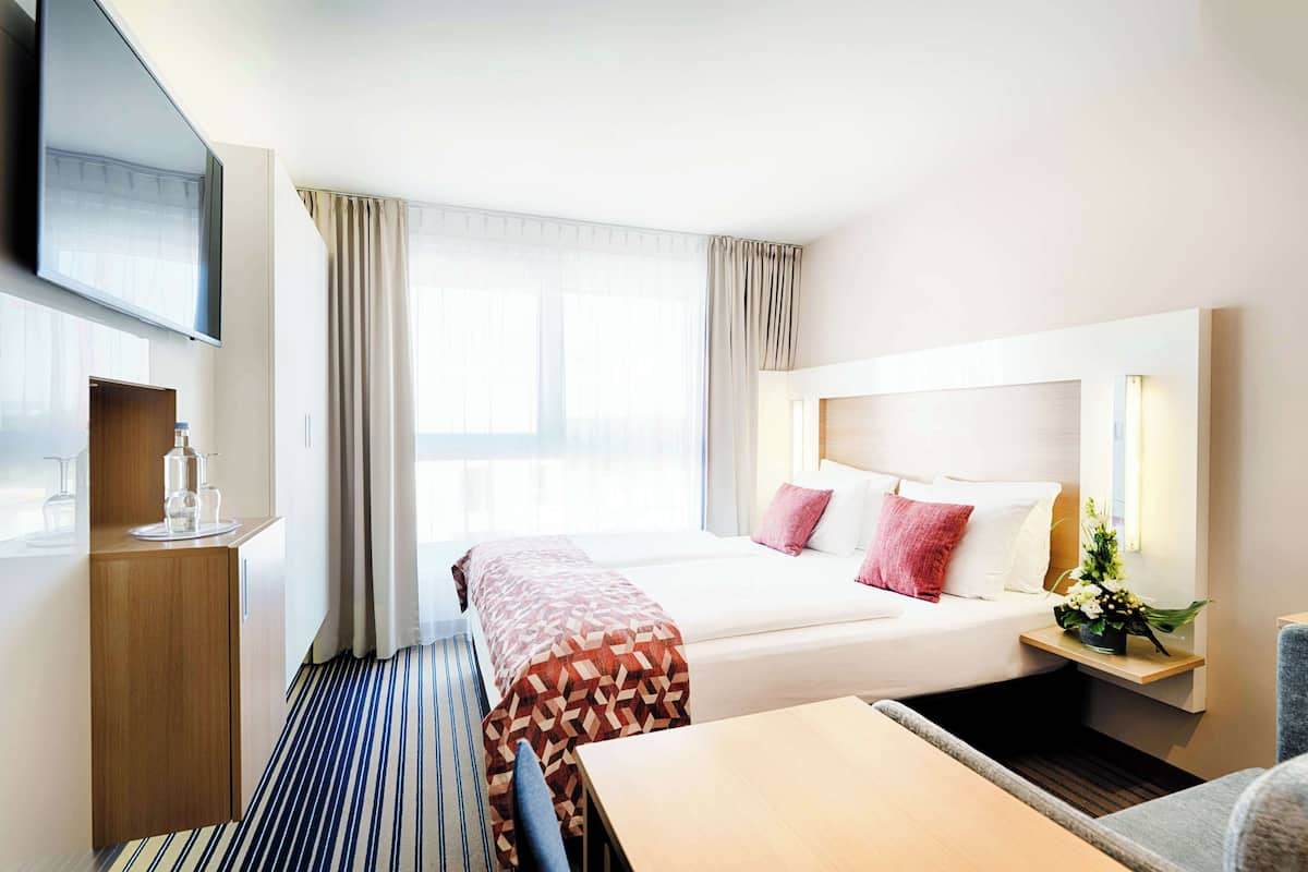 A hotel room with a bed, bedside table, TV, and a window with curtains.