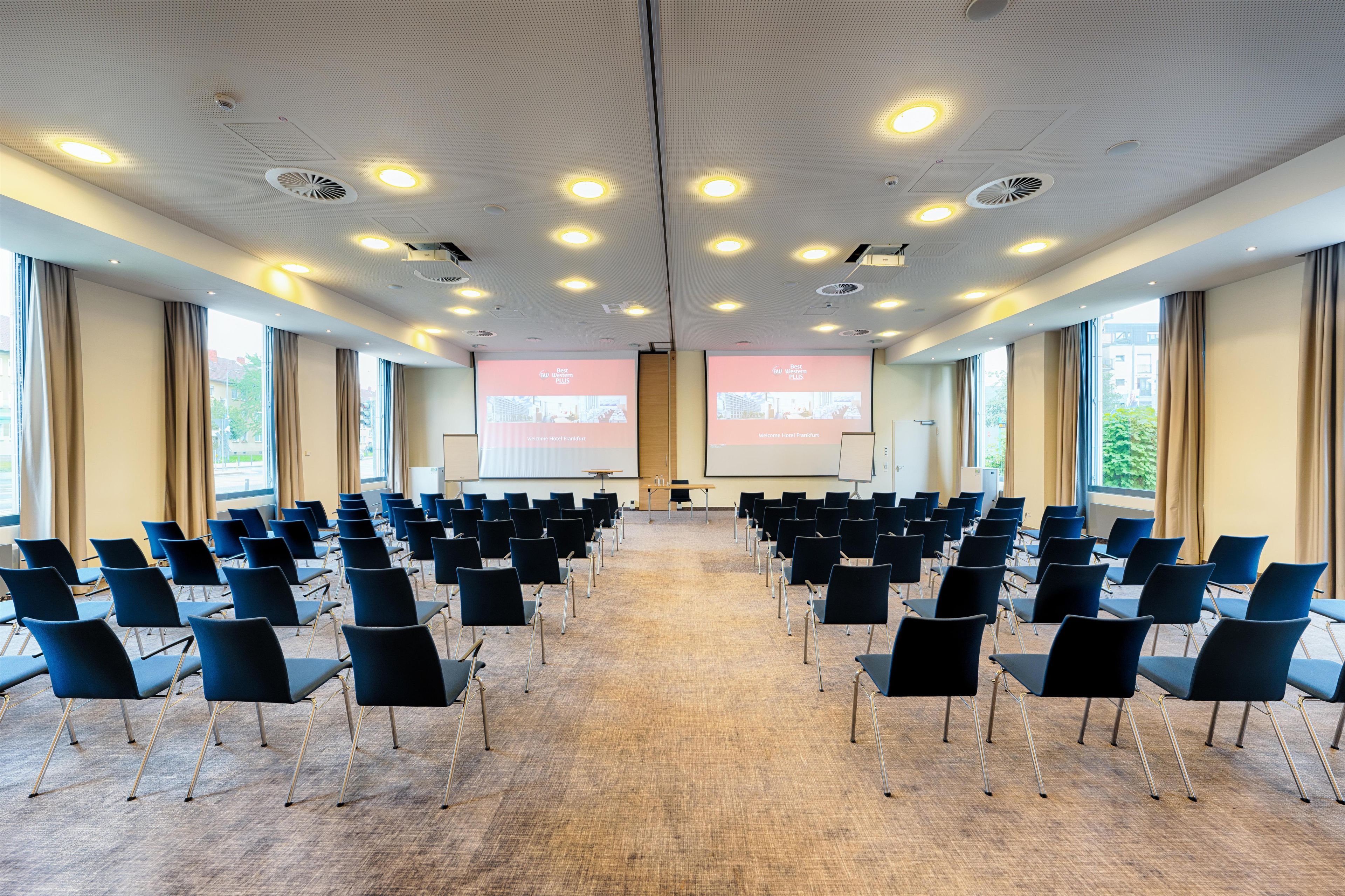 A conference room with rows of chairs, a projector screen, and a carpeted floor.