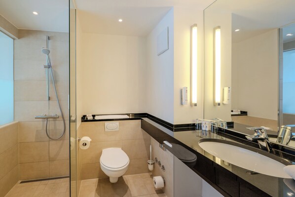 A modern bathroom with a glass-enclosed shower, a white toilet, and a large mirror with built-in lighting.