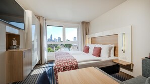 A hotel room with a bed, a desk, a chair, a TV, and a window with a city view. - Best Western Plus Welcome Hotel Frankfurt (Frankfurt)