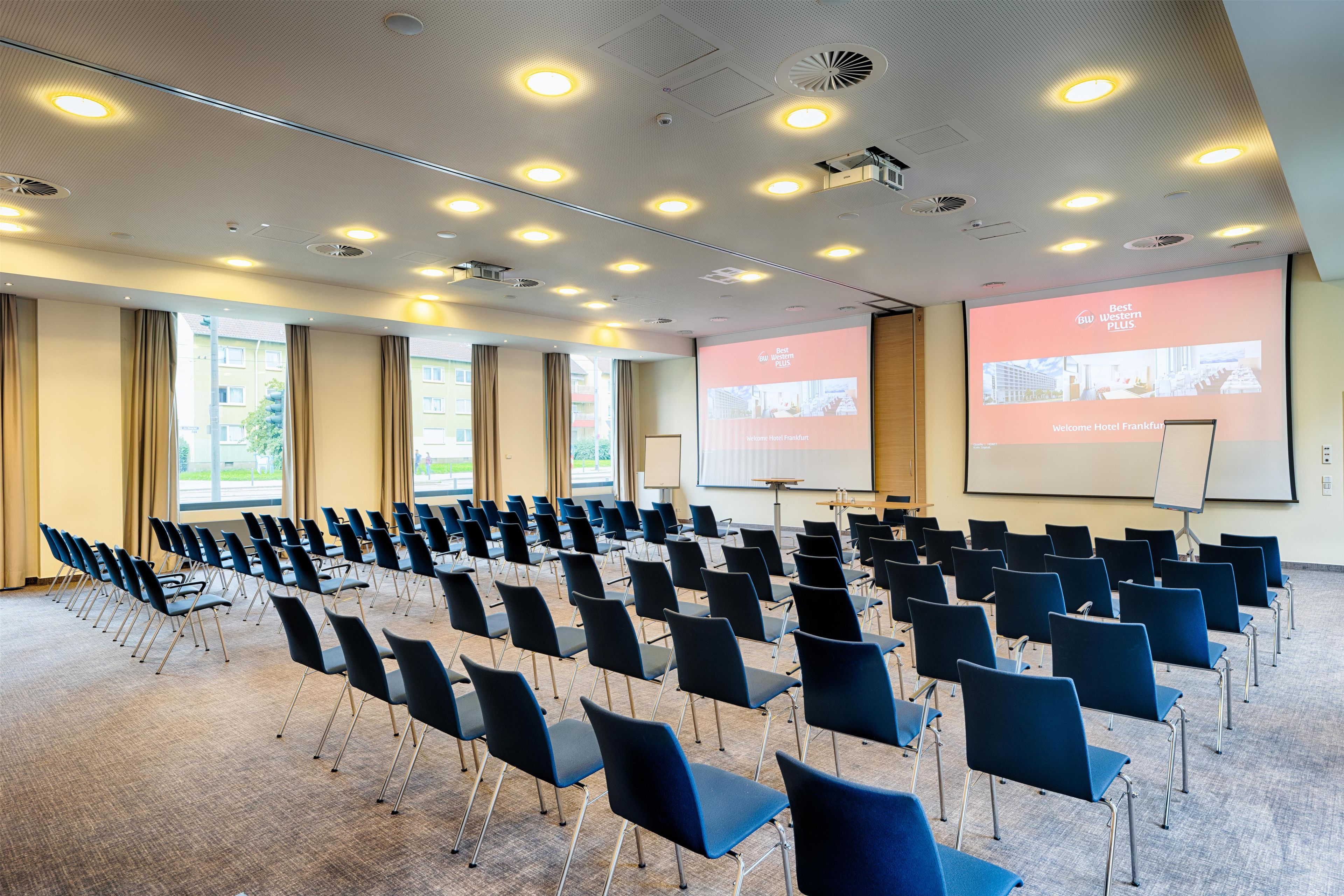 Une salle de conférence avec des rangées de chaises, un écran de projection et une présentation sur Best Western PLUS.