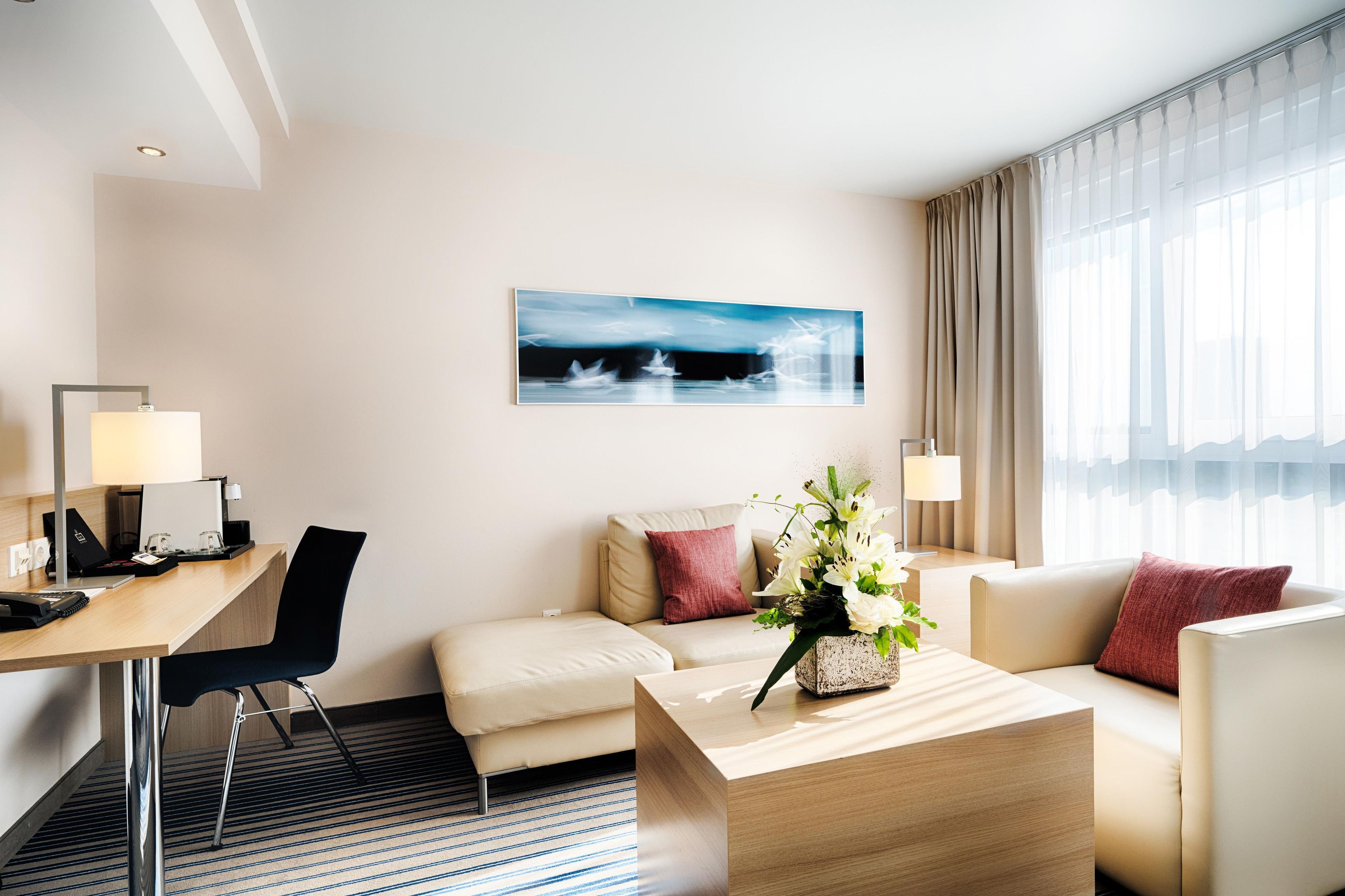 A hotel room with a desk, two chairs, a sofa, a coffee table, and a painting on the wall.