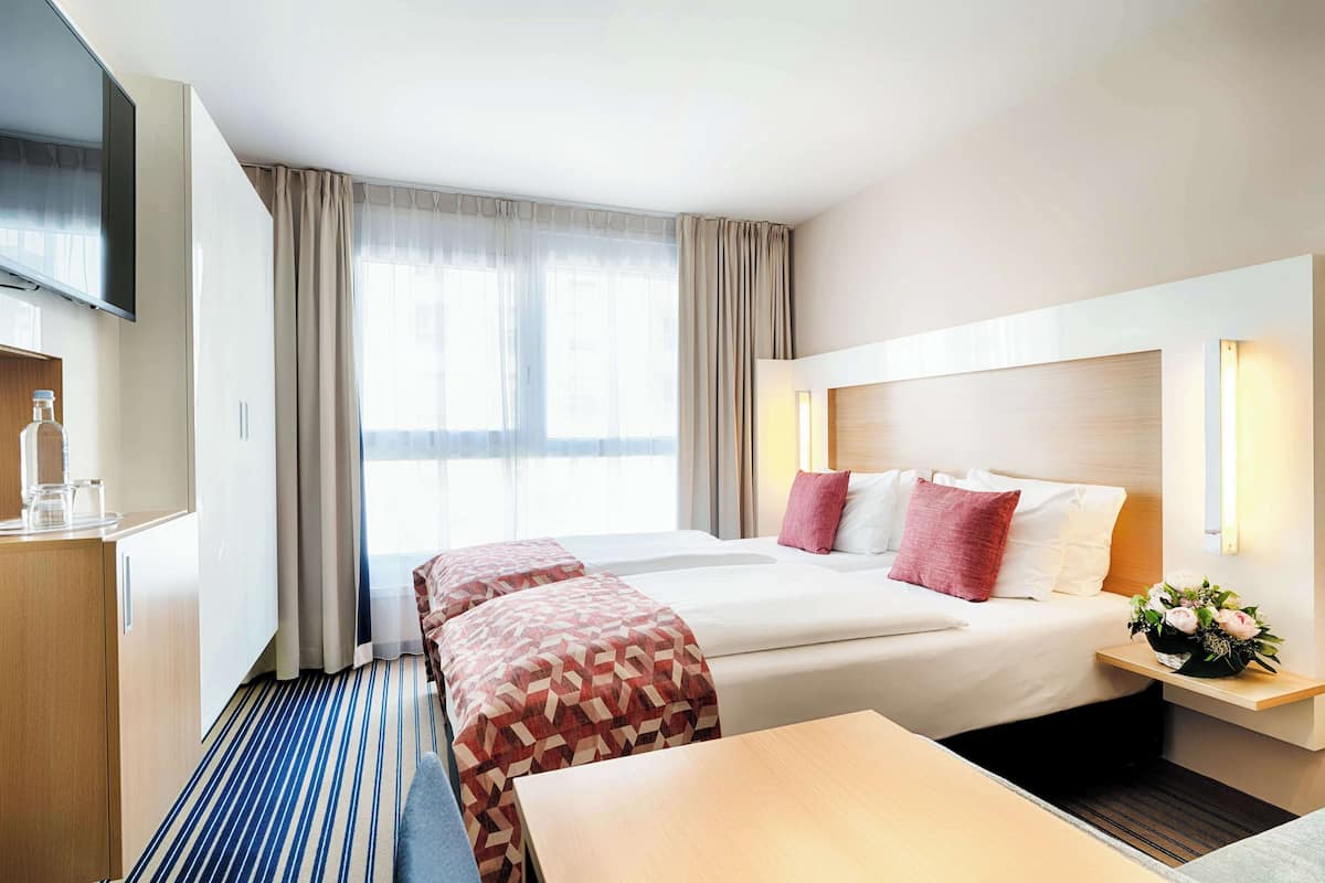 A hotel room with a large bed, a TV, a desk, and a window with curtains.