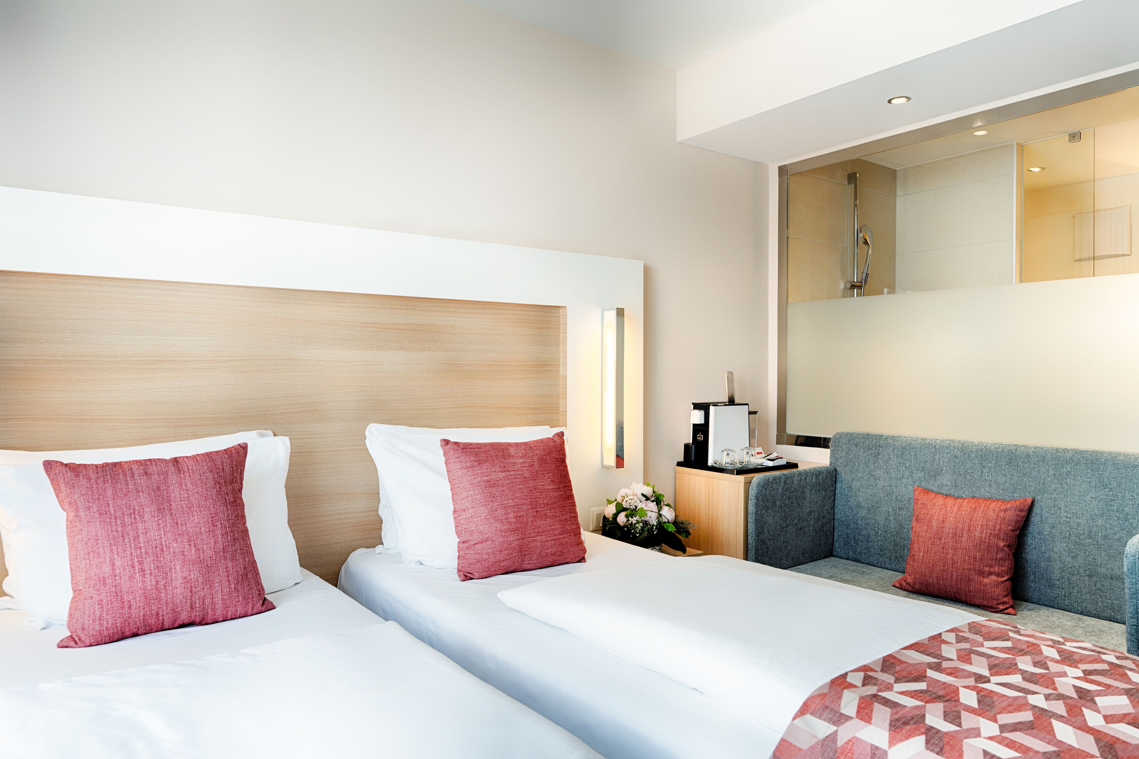 Ein Hotelzimmer mit zwei Betten, einer Couch, einer Kaffeemaschine und einer Duschkabine.