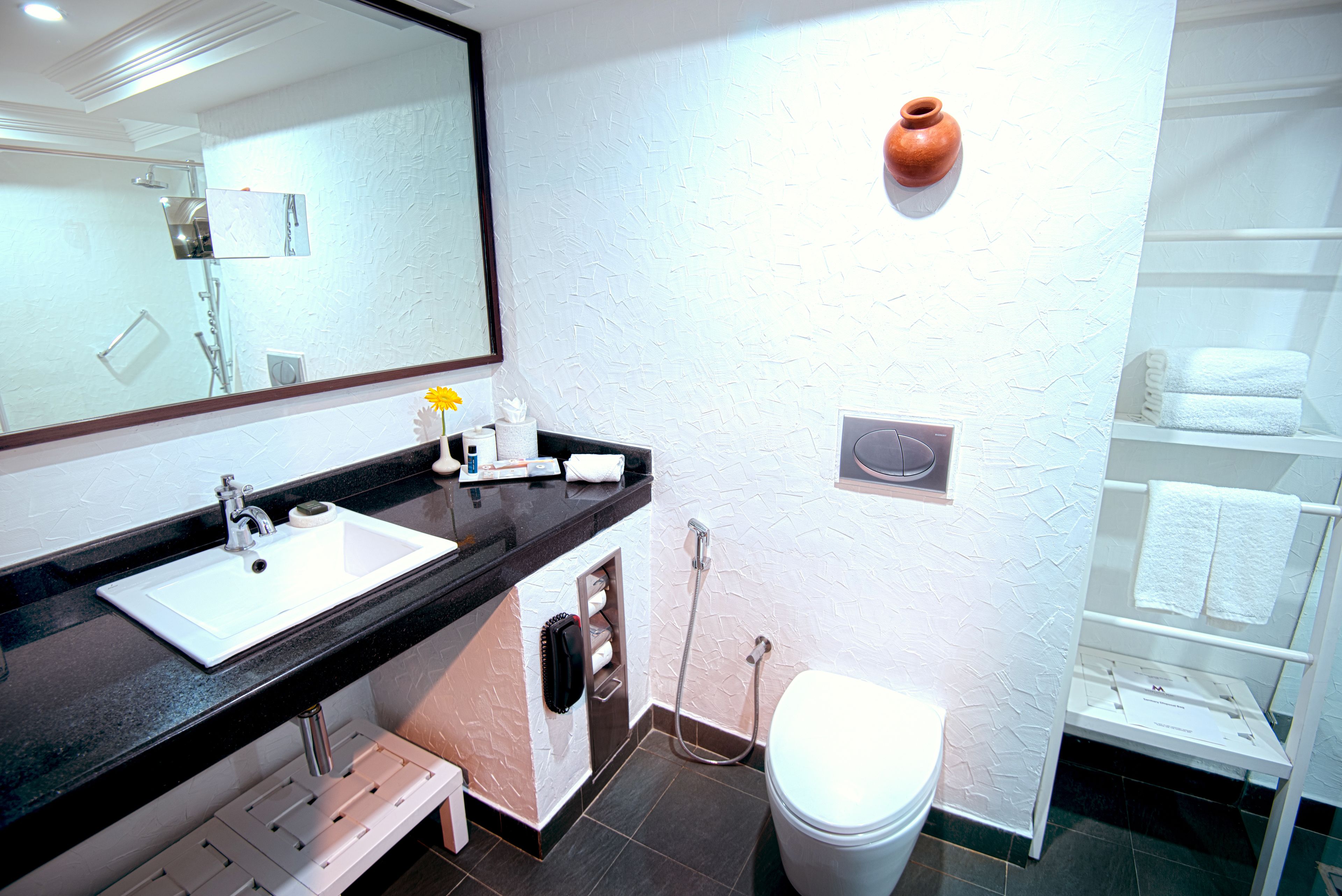 Ein Badezimmer mit weißem Waschbecken, Spiegel und Toilette. Ein Handtuchhalter und eine kleine Ablage mit Toilettenartikeln sind vorhanden.