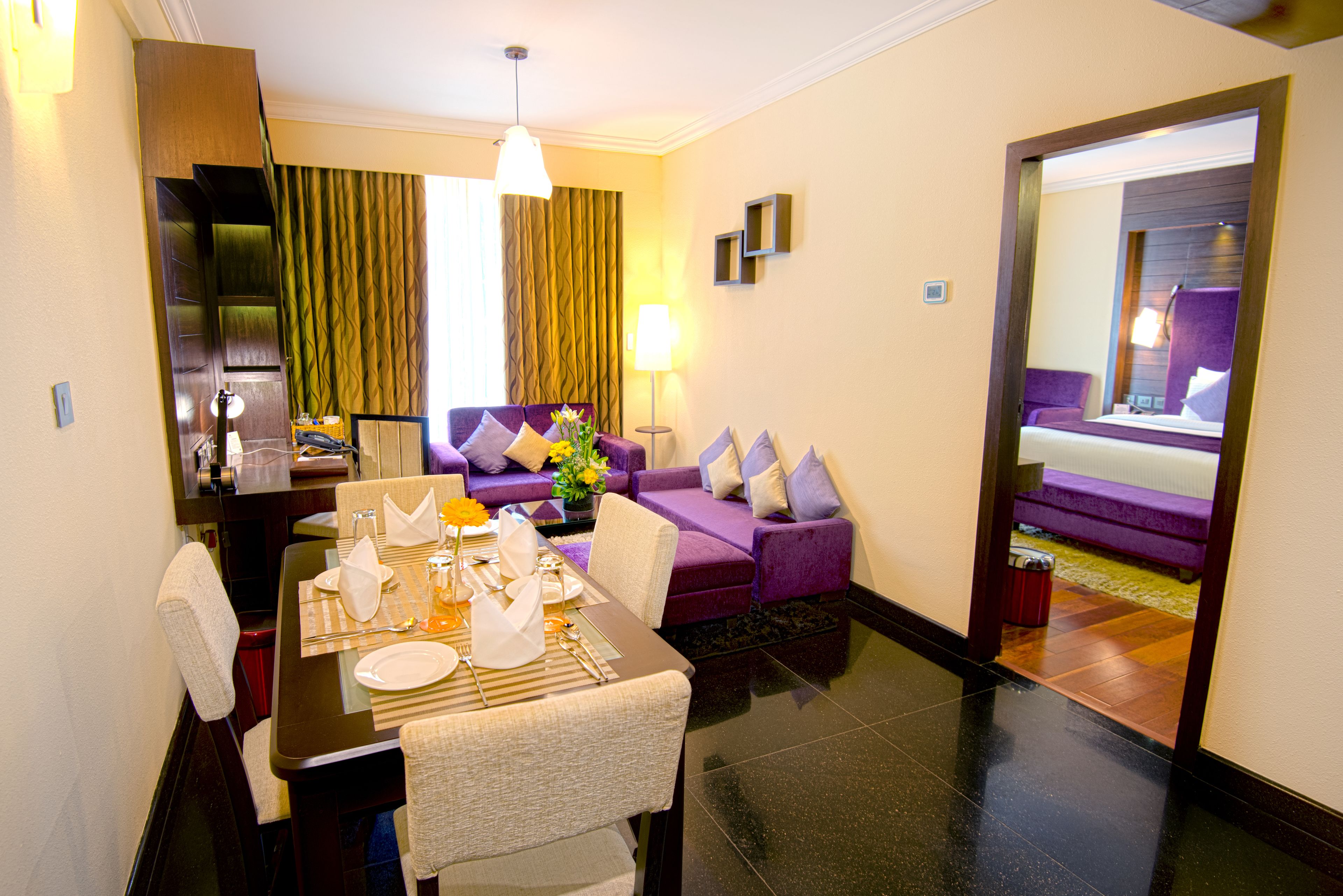 Habitación de hotel con comedor, un sofá, un espejo y vista a otra habitación.