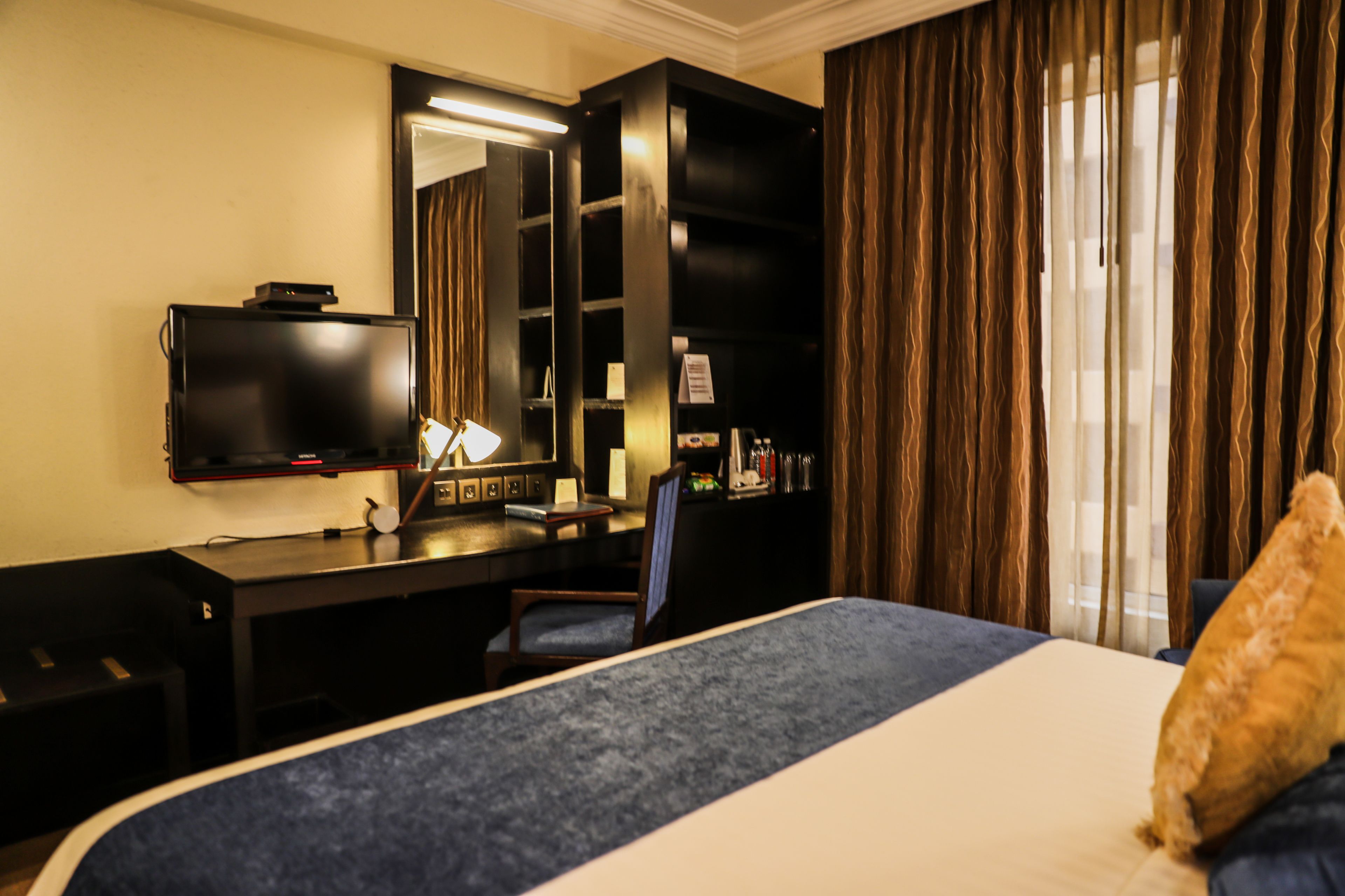 Habitación de hotel con cama, escritorio con computadora, silla, televisor y estantería.