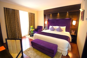 A hotel room with a large bed, a chair, a bench, and a nightstand with a lamp. - Sterlings Mac Hotel (Bengaluru)