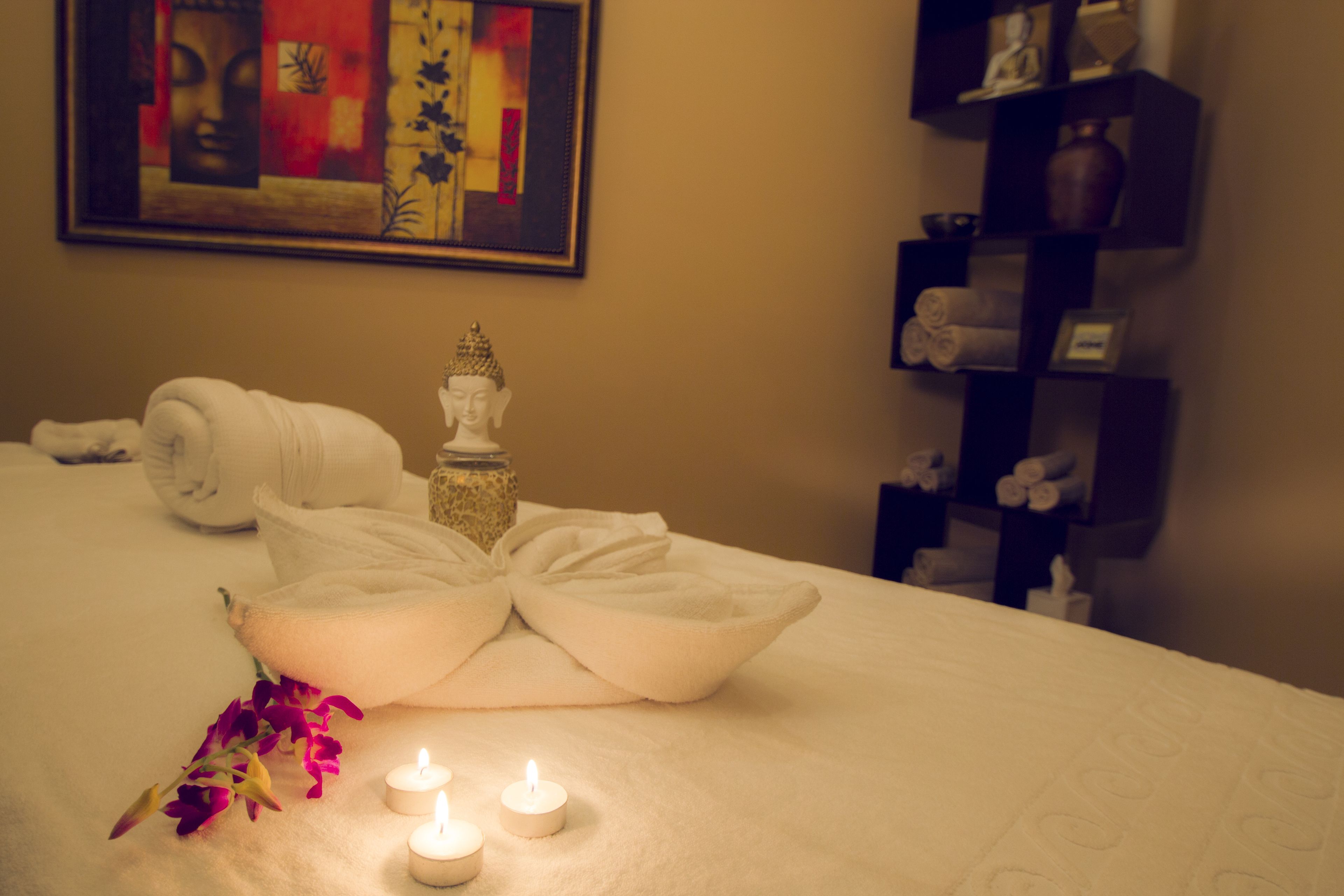 A neatly made bed with towels, a decorative Buddha statue, and two lit candles.