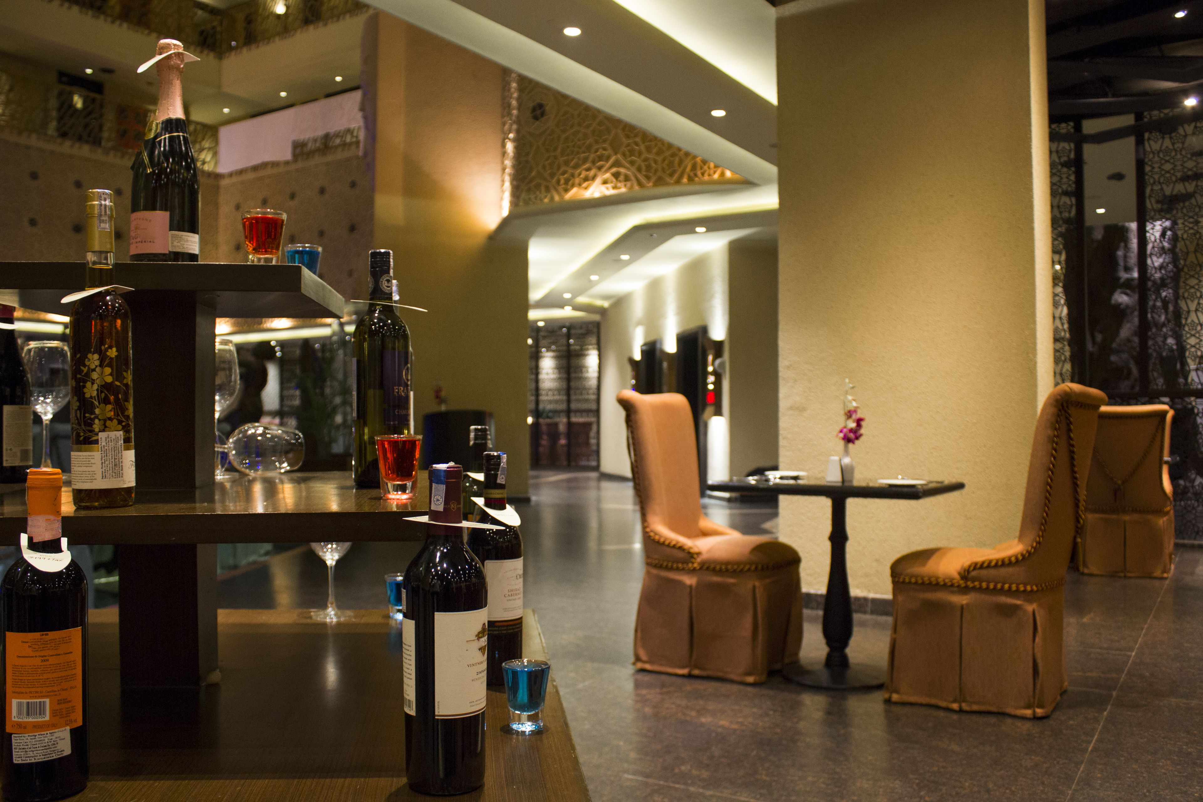 A bar area with multiple bottles of wine, glasses, and a seating area with cushioned chairs.
