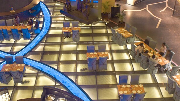 A hotel lobby with a central circular seating area, multiple dining tables, and a staircase leading to an upper level. - Sterlings Mac Hotel (Bengaluru)