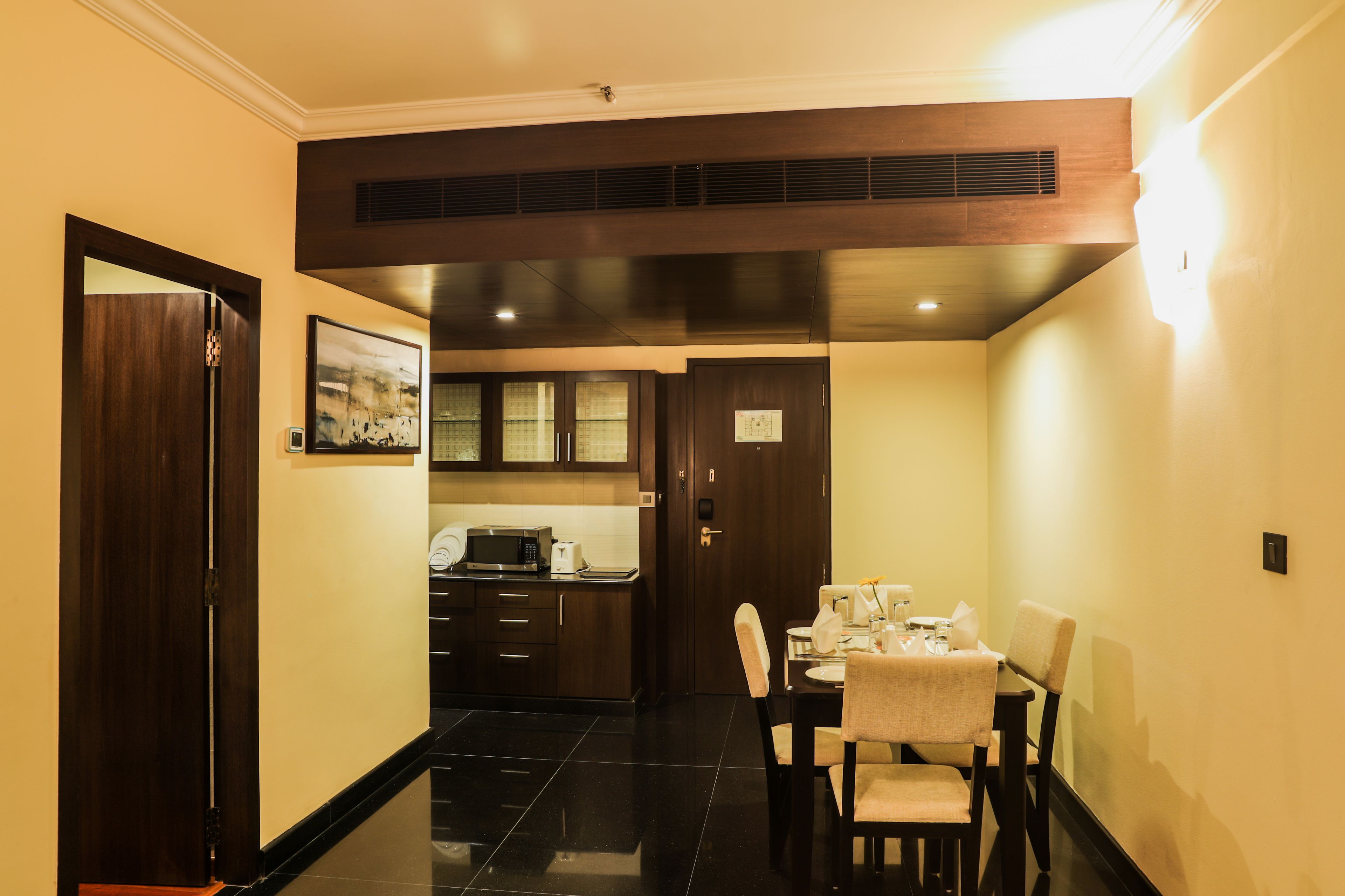 A hotel room with a dining area, a kitchen, and a separate entrance door.