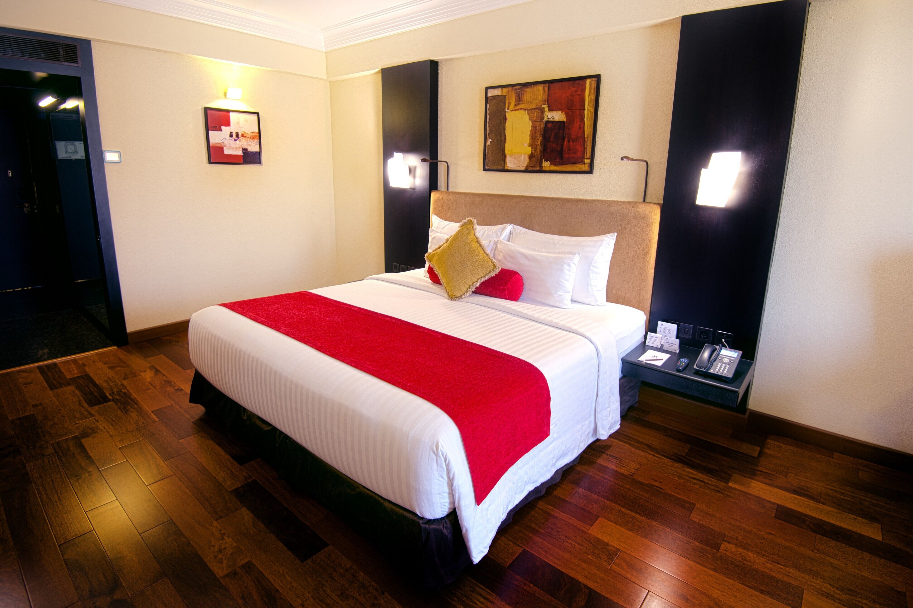 A hotel room with a large bed, wooden flooring, a nightstand with a phone, and a painting on the wall.