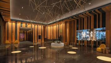 A spacious lobby with a polished floor, a reception desk, and a seating area with round tables and chairs.
