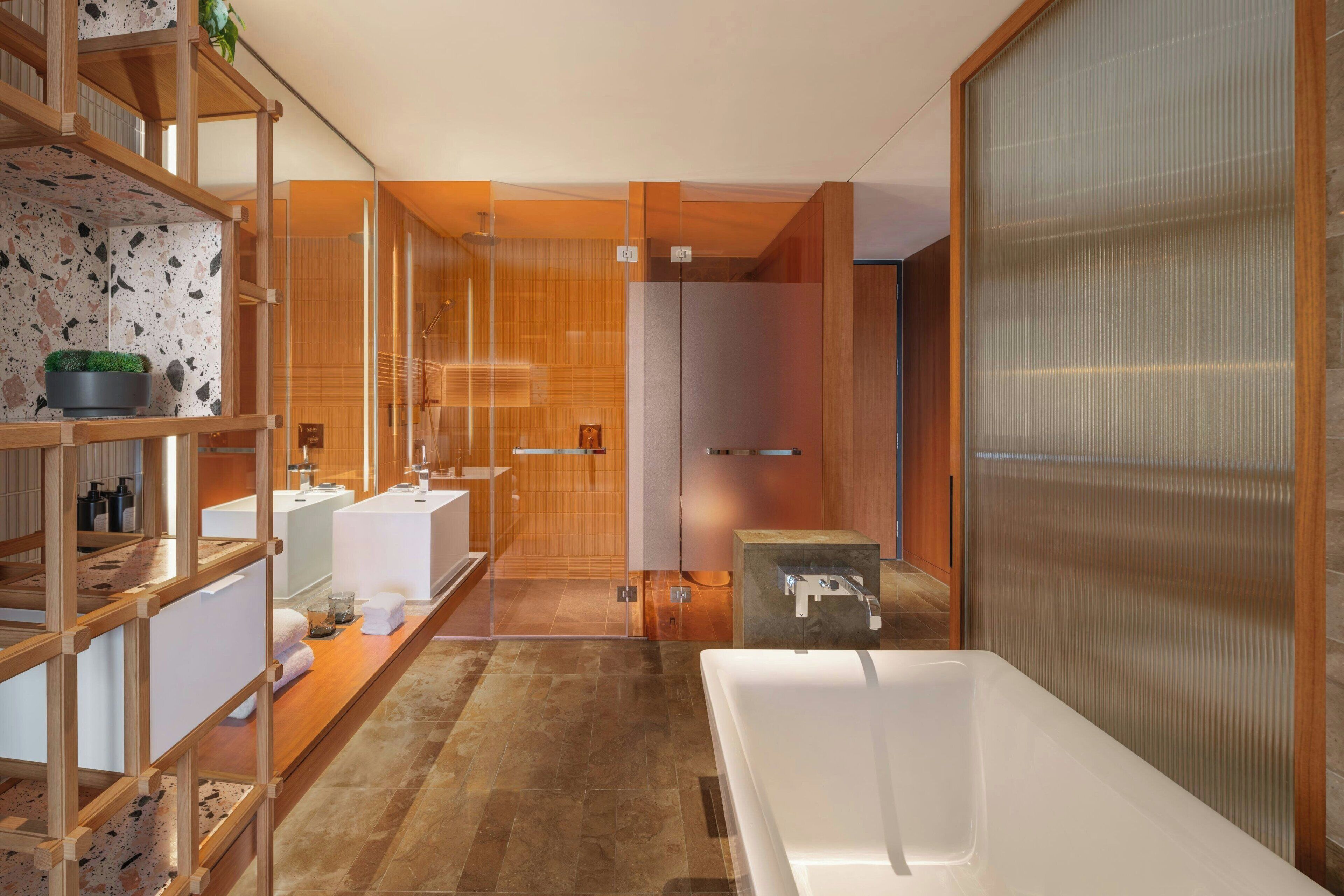 A modern bathroom with a large bathtub, wooden shelving with toiletries, and a glass shower enclosure.