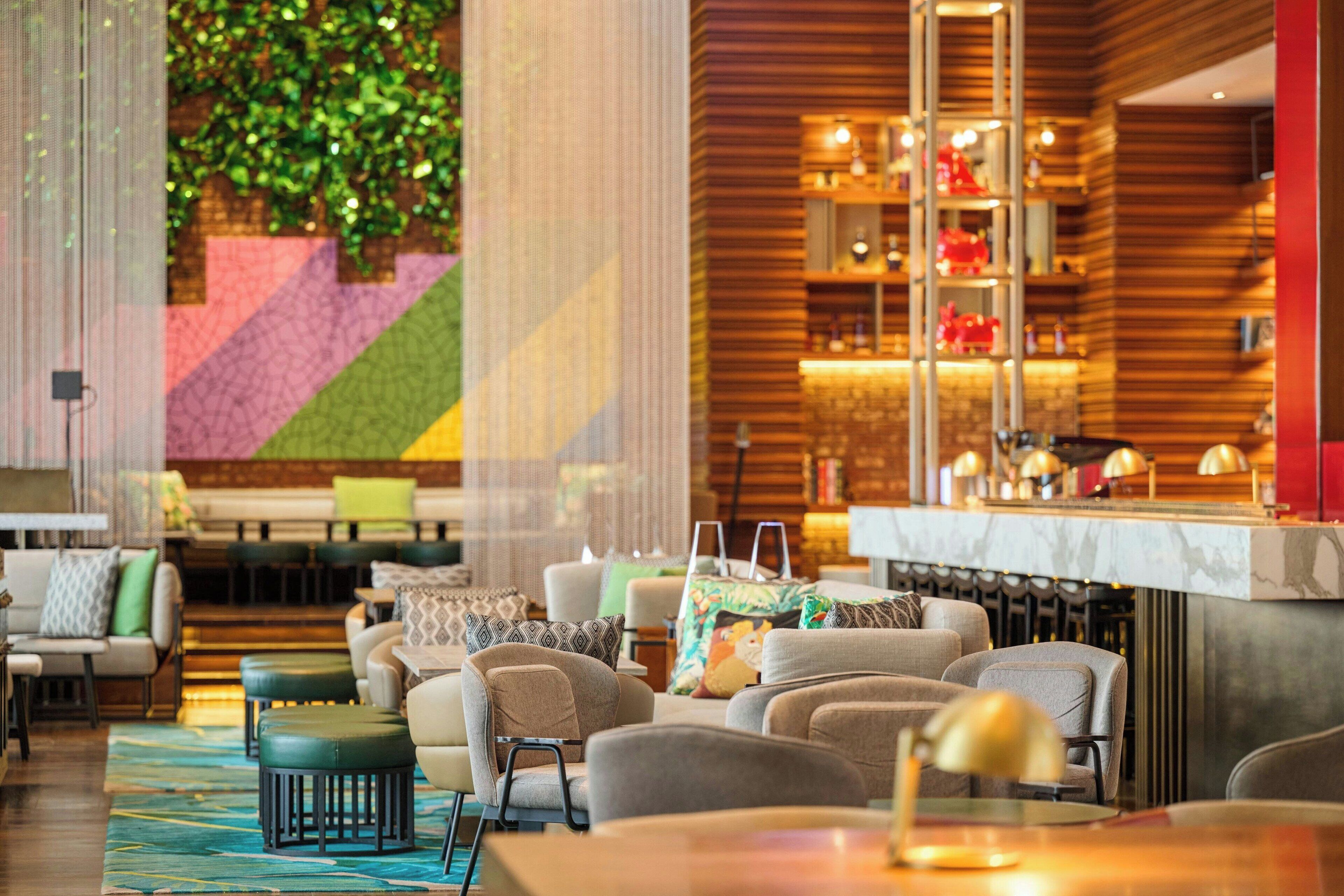 A modern hotel lobby with a bar area, seating arrangements, and a decorative wall with greenery.