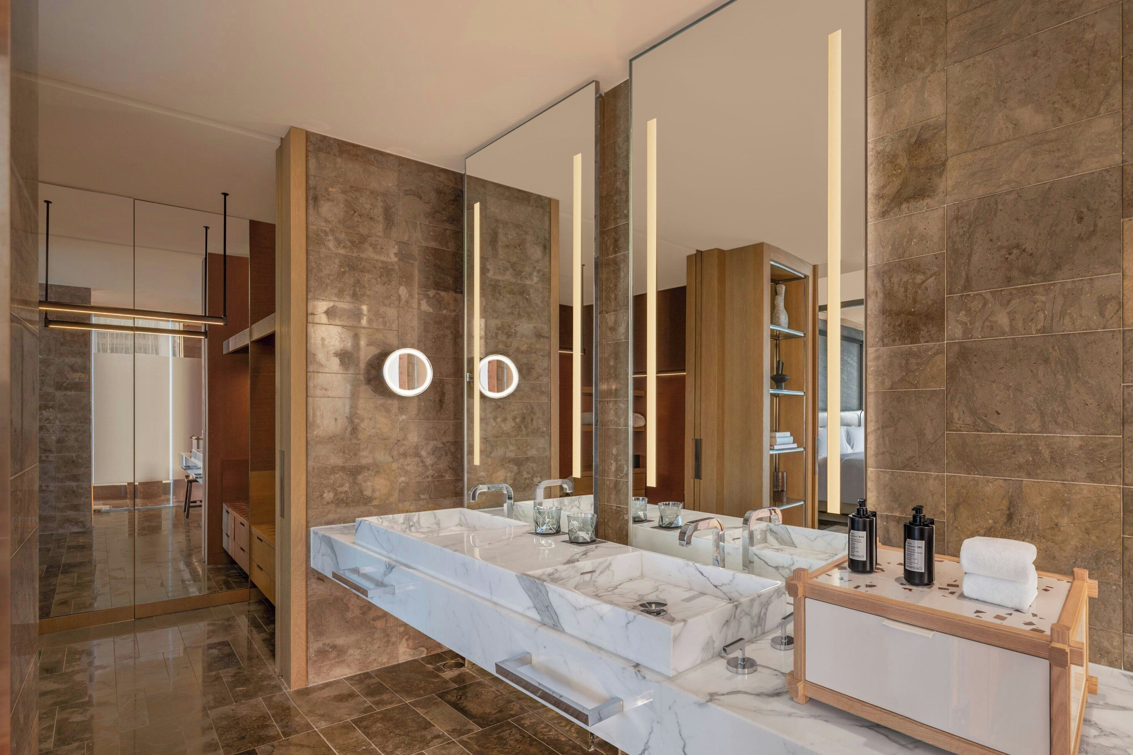 A modern bathroom with a marble sink, two mirrors, and a wooden vanity.