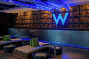 A modern lounge area with a large illuminated 'W' sign, cushioned seating, and a wall of stacked logs.