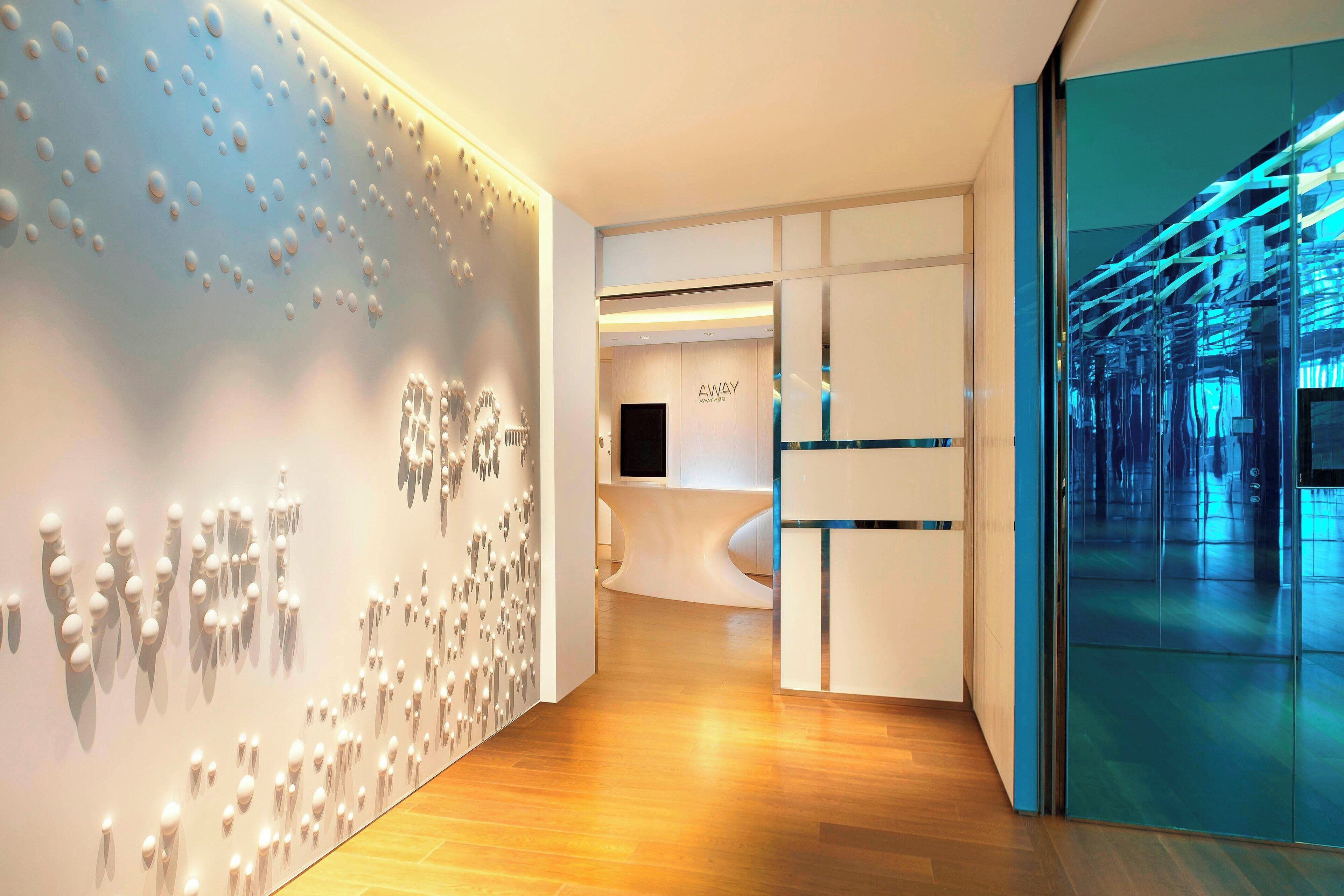A modern hotel lobby with a wooden floor, a reception desk, and a wall with a unique light fixture.