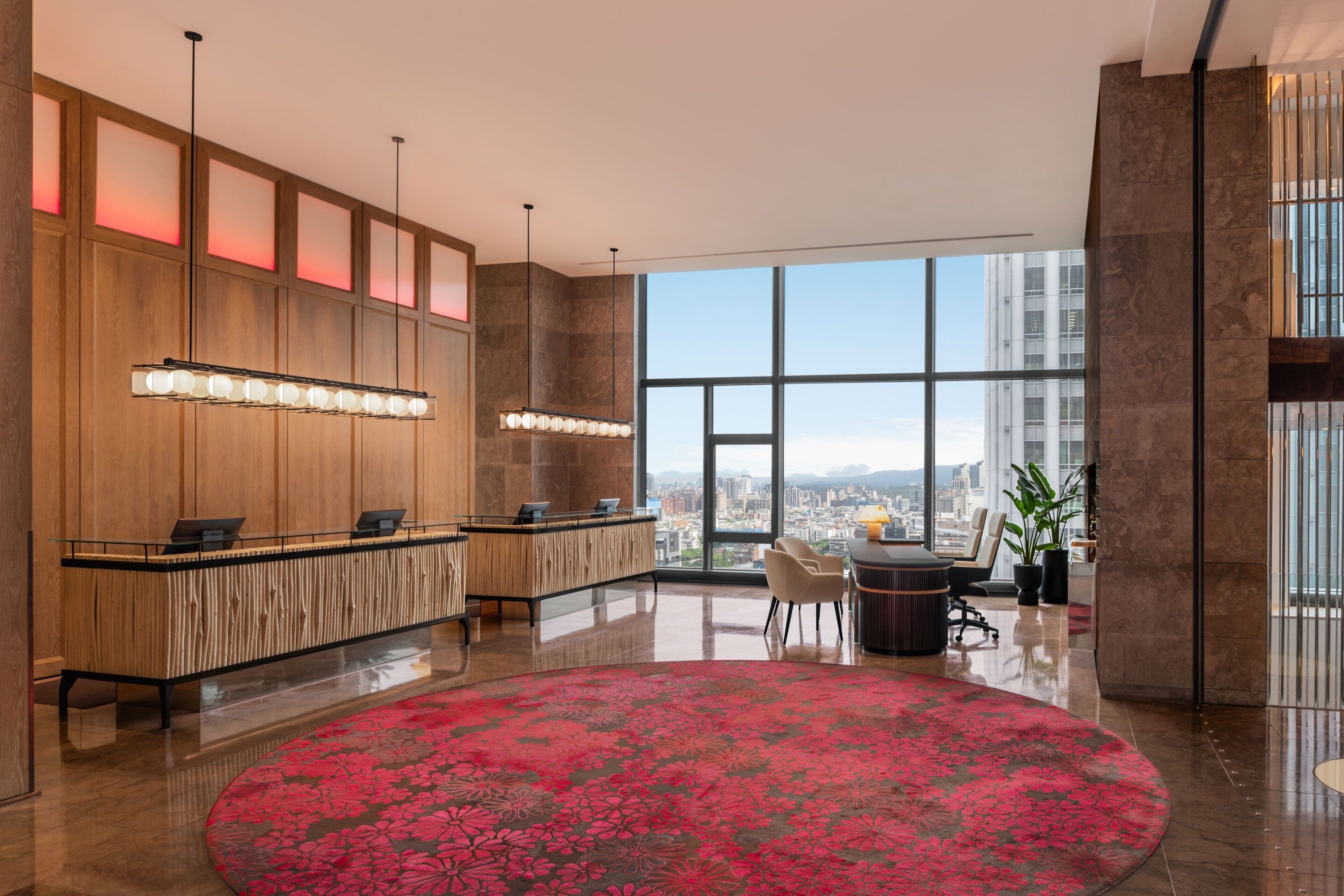 Un moderno vestíbulo de hotel con mostrador de recepción, zona de estar y amplios ventanales con vistas a la ciudad.
