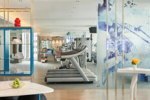 A modern gym with treadmills, exercise equipment, and a glass display case with towels.