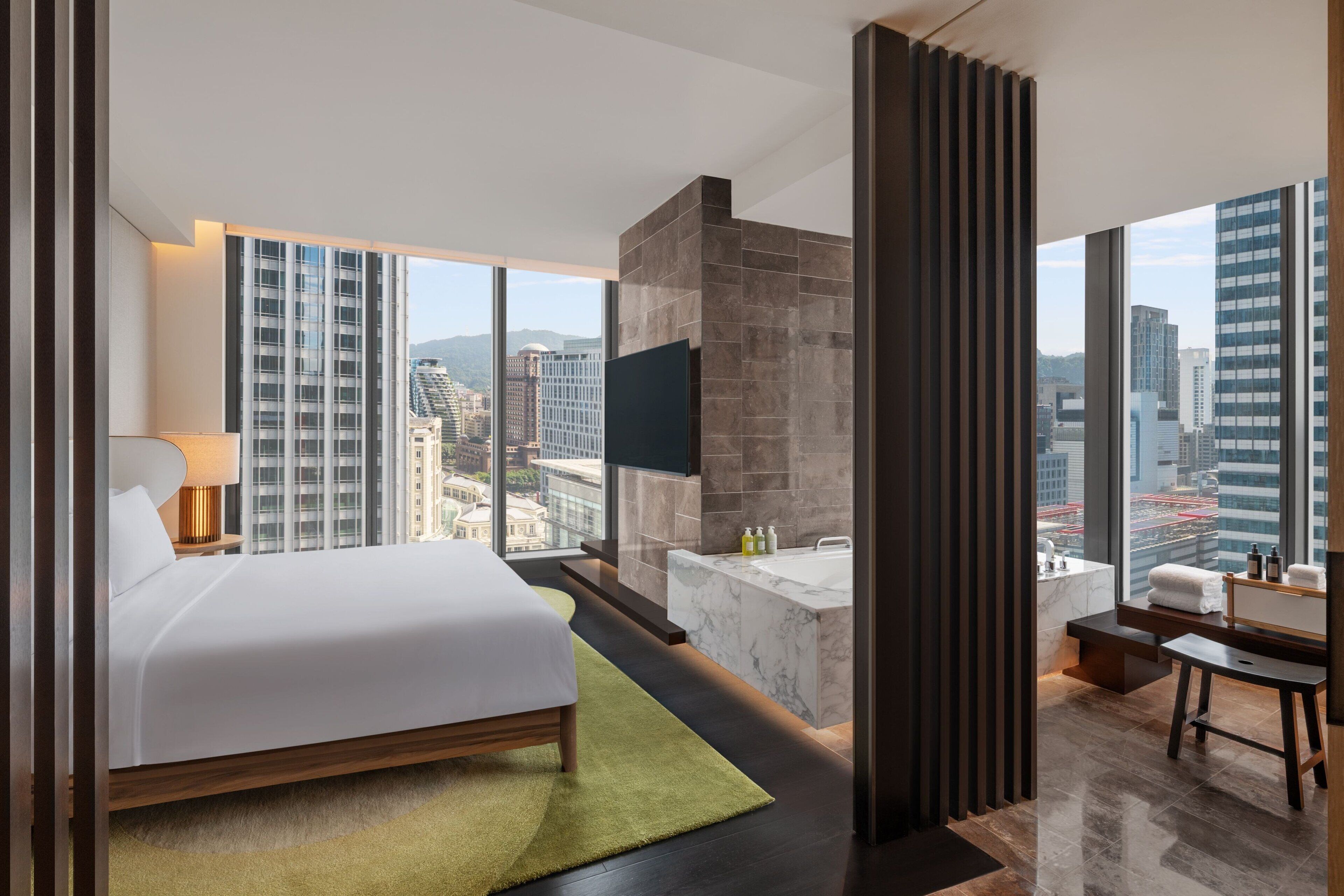 Una habitación de hotel moderna con una cama grande, una zona de estar, una bañera y vistas a la ciudad.