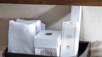 Un meuble-lavabo de salle de bain avec un miroir, une serviette blanche, un savon brun et une boîte blanche portant l’inscription « Hôtel Epoque ».