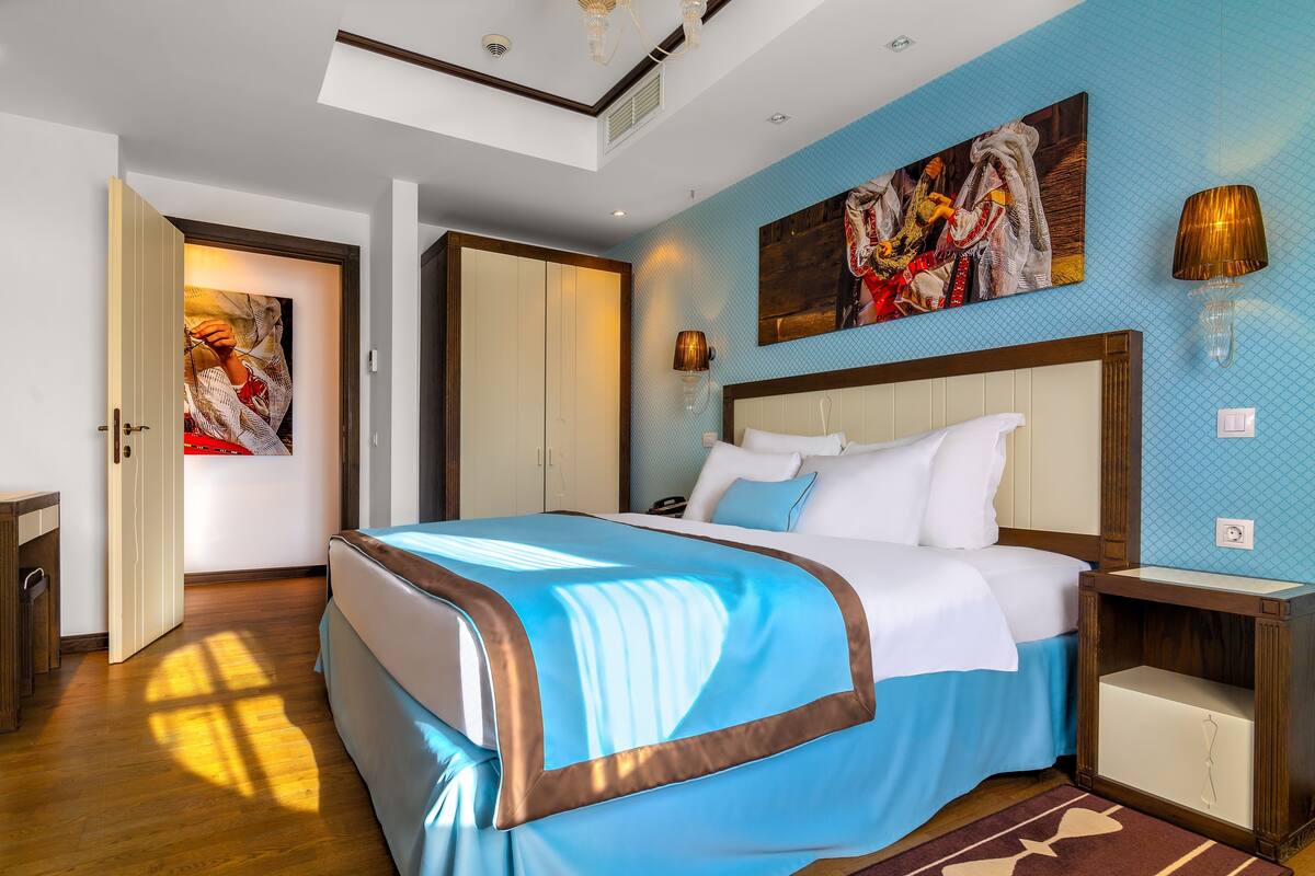 A hotel room with a large bed, a wardrobe, a nightstand, and a painting on the wall.