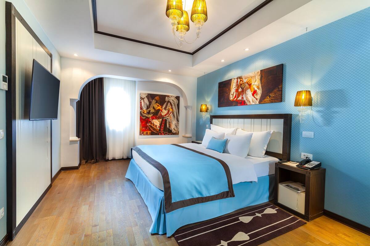 A modern hotel room with a large bed, a flat-screen TV, and artwork on the walls.