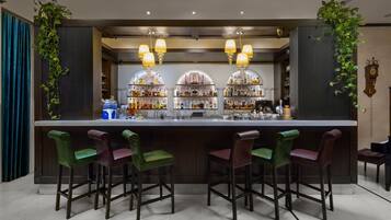 A bar area with a long counter, multiple bar stools, and shelves stocked with bottles.