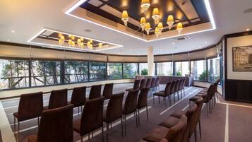 Un salón de conferencias con filas de sillas, una mesa grande y una lámpara moderna.