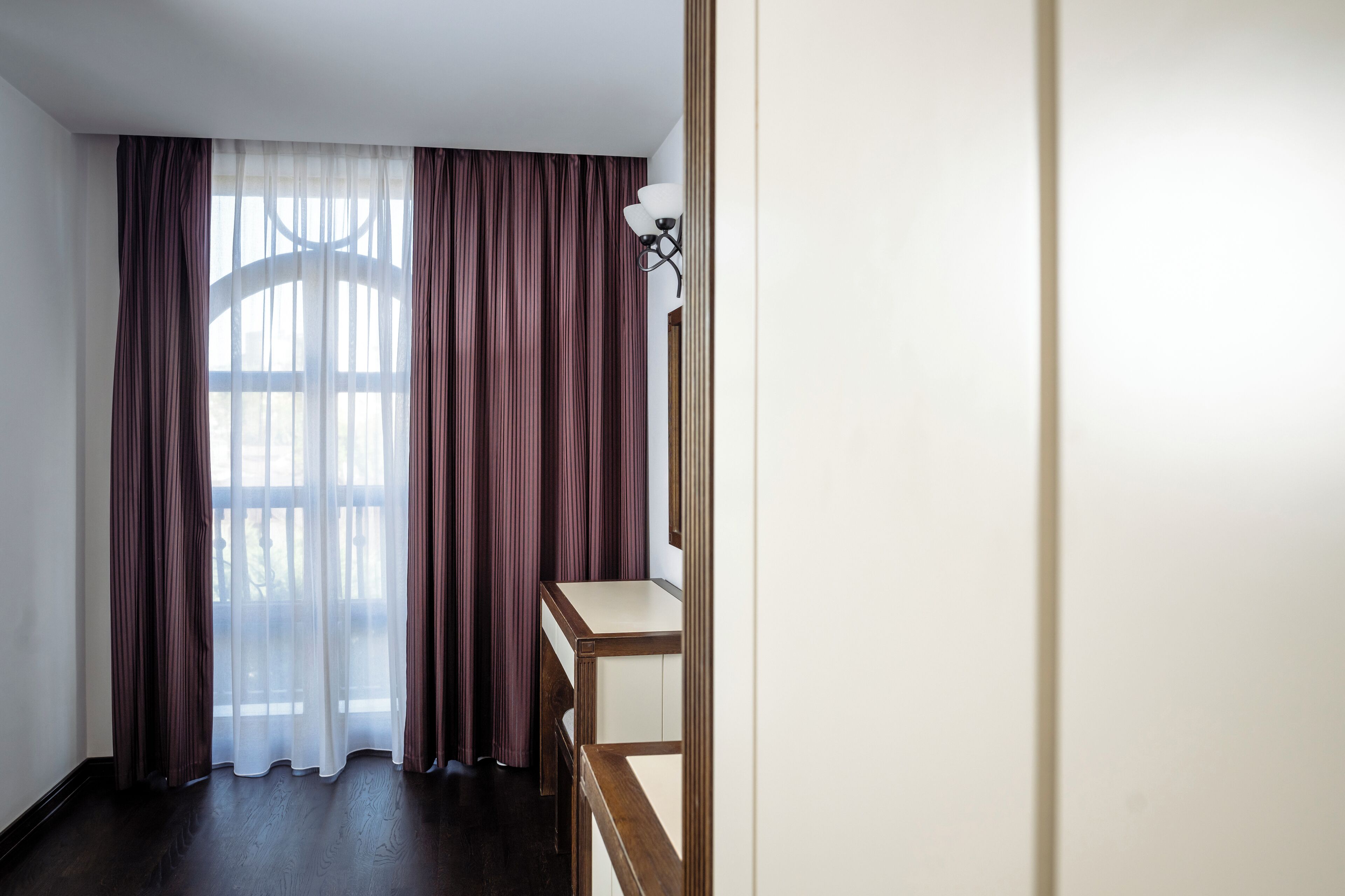 A room with a large window, a wooden desk, and a light fixture.