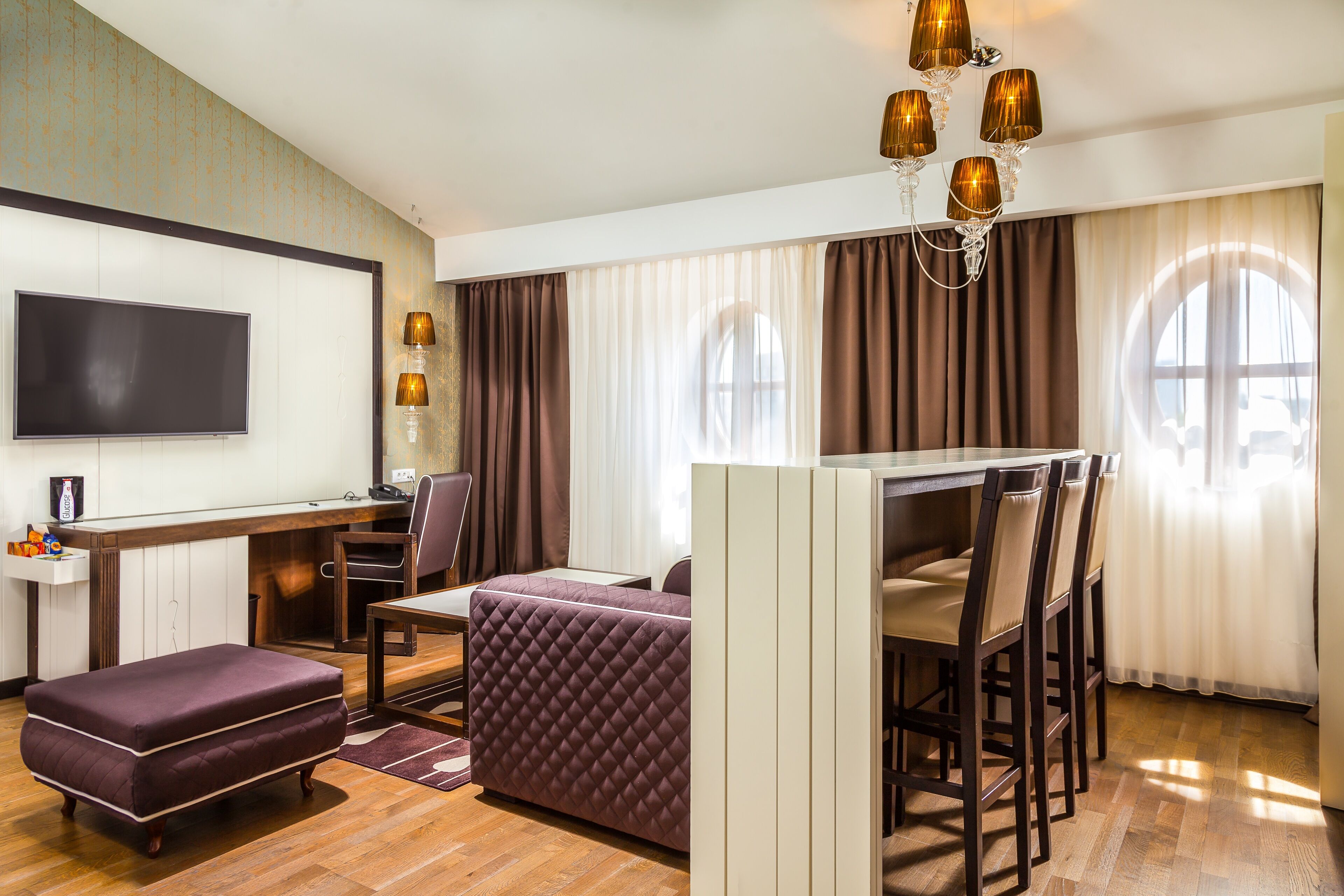 Une chambre d’hôtel moderne dotée d’une télévision à écran plat, d’un coin repas avec une table et des chaises, d’un canapé et d’un lustre.