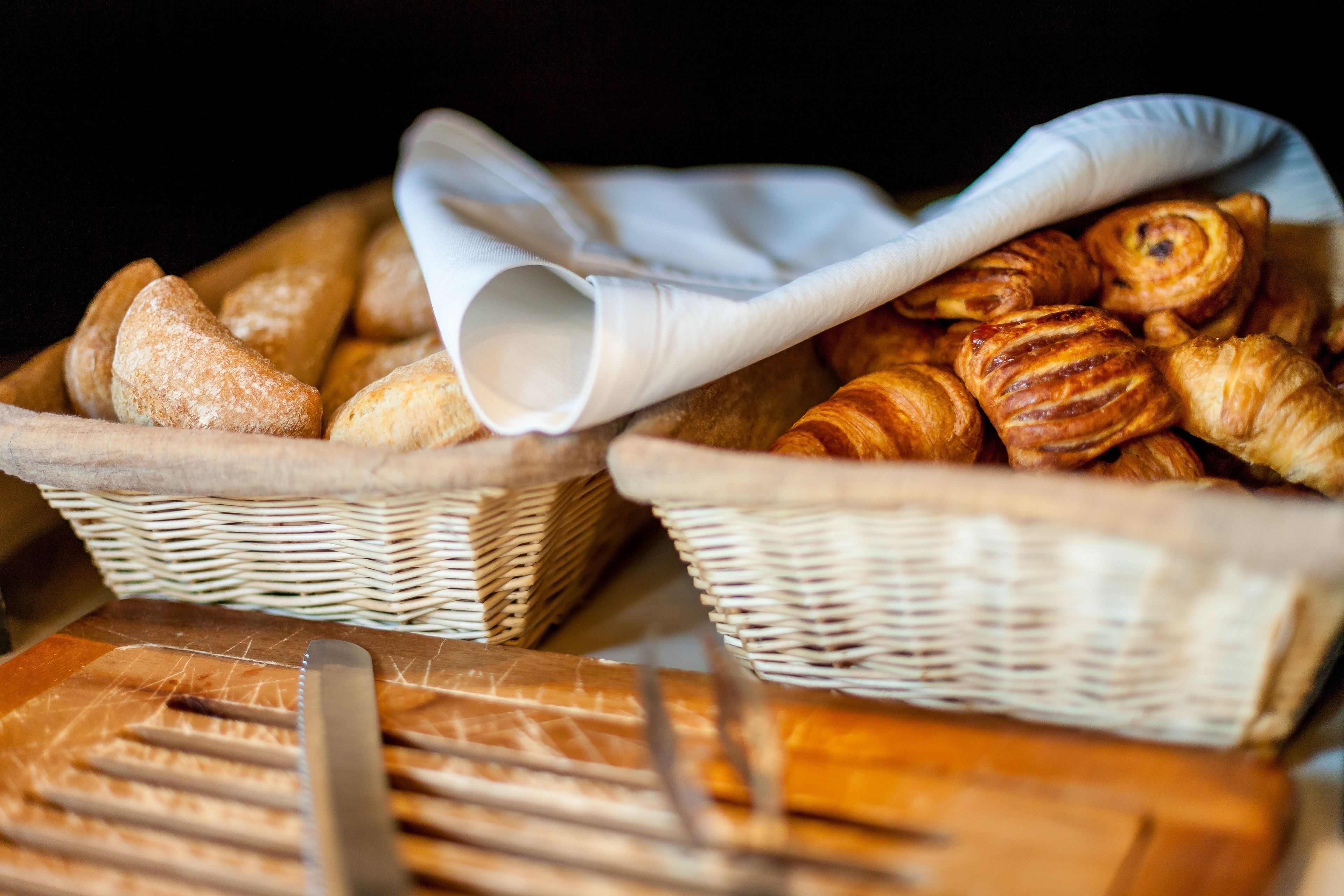 Two wicker baskets filled with various types of bread, including croissants and baguettes, placed on a wooden surface.