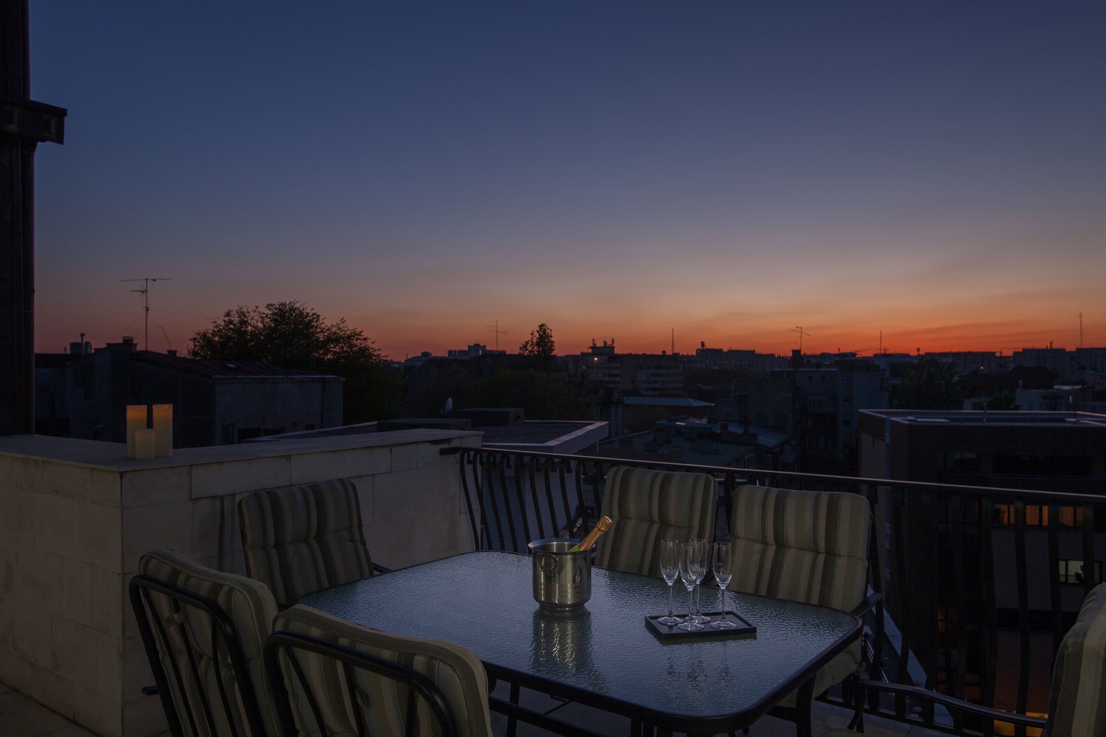 A rooftop terrace with a table and chairs, a bottle of champagne, and three glasses.
