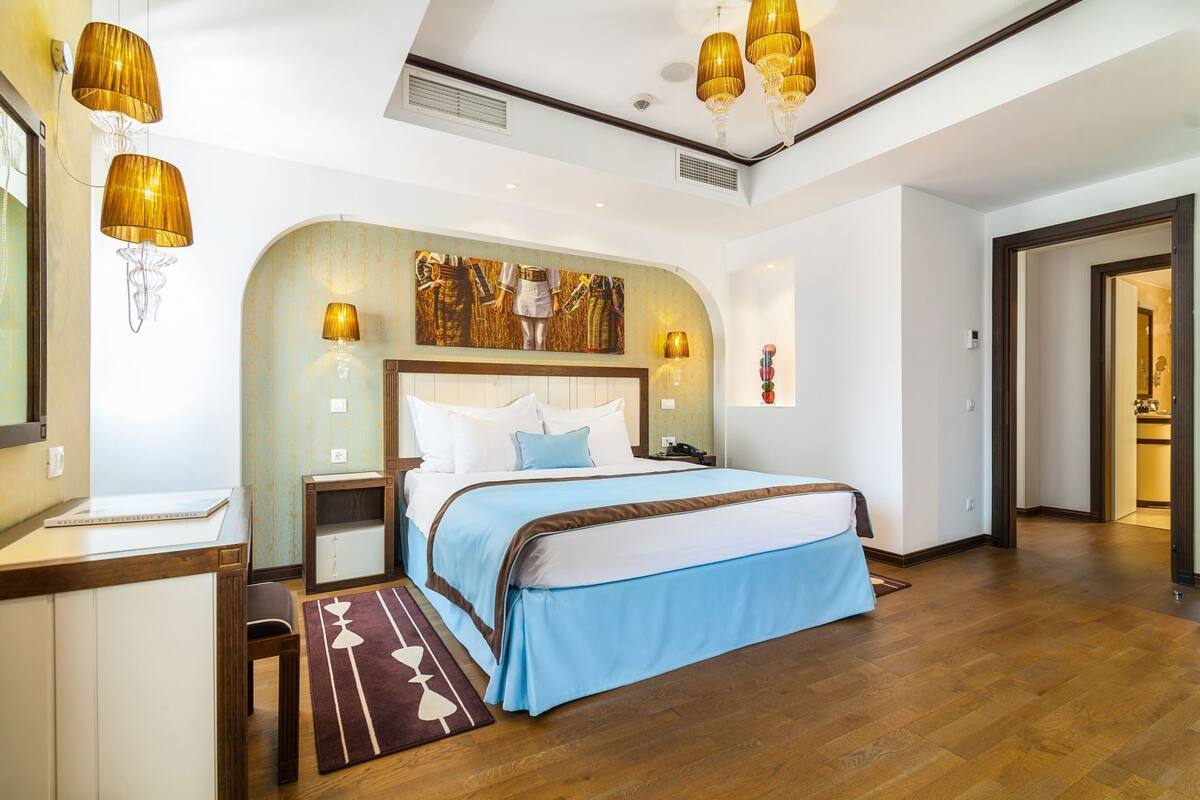 A hotel room with a large bed, a desk, a chair, a rug, and a mirror.