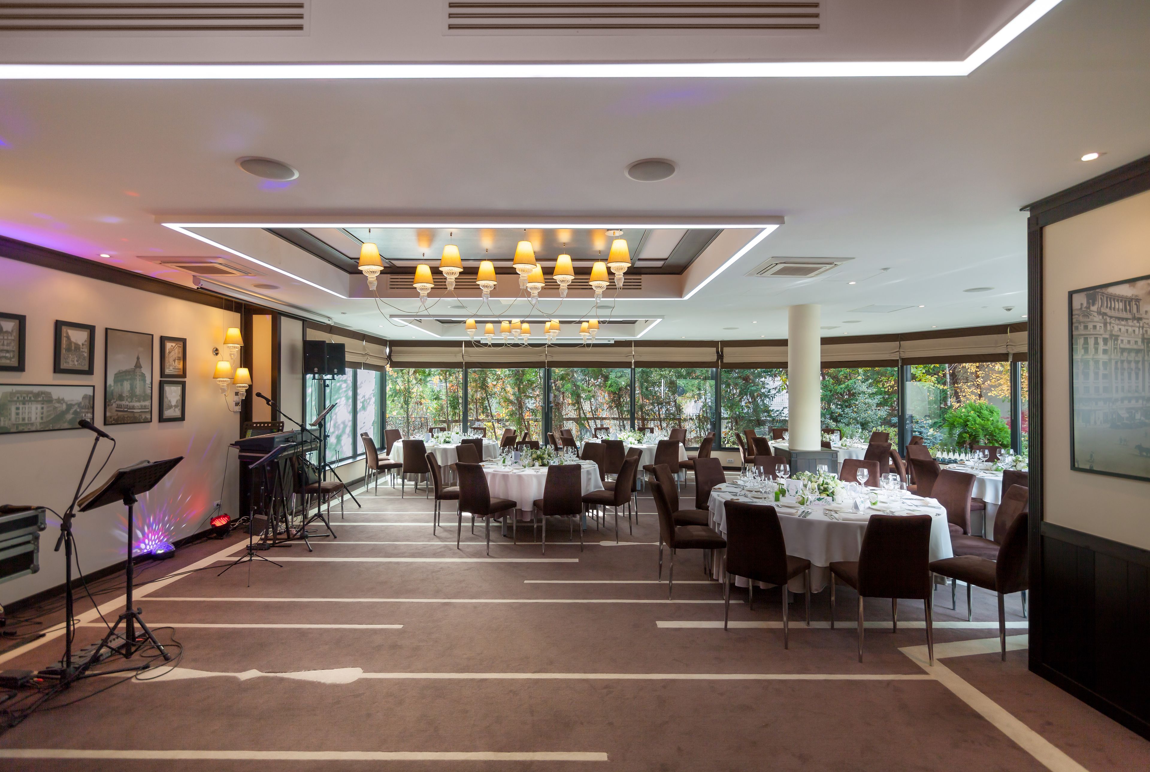 A spacious dining area with multiple tables set for guests, large windows offering a view of the outdoors, and a stage with musical equipment.