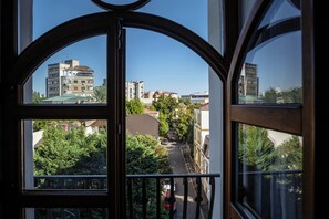 A view from a window with a balcony, overlooking a street lined with buildings and trees.