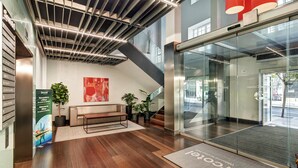 A modern reception area with a bench, potted plants, a glass elevator, and a welcome mat. - Hotel Sercotel Coliseo (Bilbao)