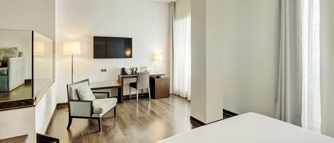 Habitación de hotel con cama, escritorio, silla, televisor y un gran ventanal con cortinas.