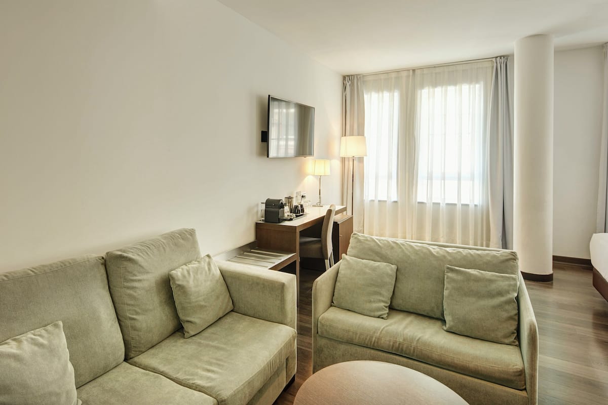 Ein Hotelzimmer mit einer Couch, einem Schreibtisch mit Lampe, einem Bett und einem Fernseher.