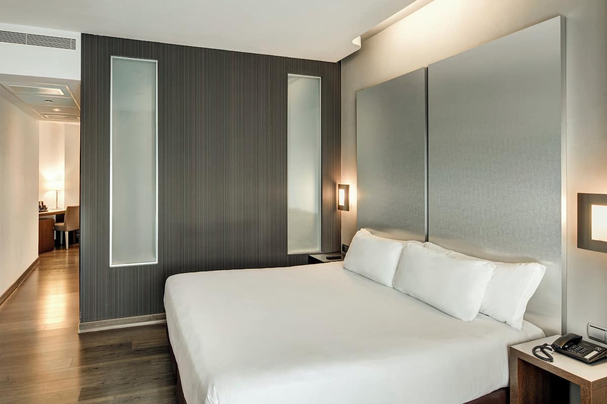 Ein Hotelzimmer mit einem großen Bett, einem Schreibtisch, einem Stuhl, einem Fernseher und einer Tür mit Milchglasfenster.