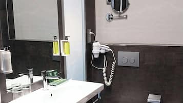 Un baño moderno con un espejo grande, un lavabo con tocador, un inodoro, un bidé y un secador de pelo montado en la pared.