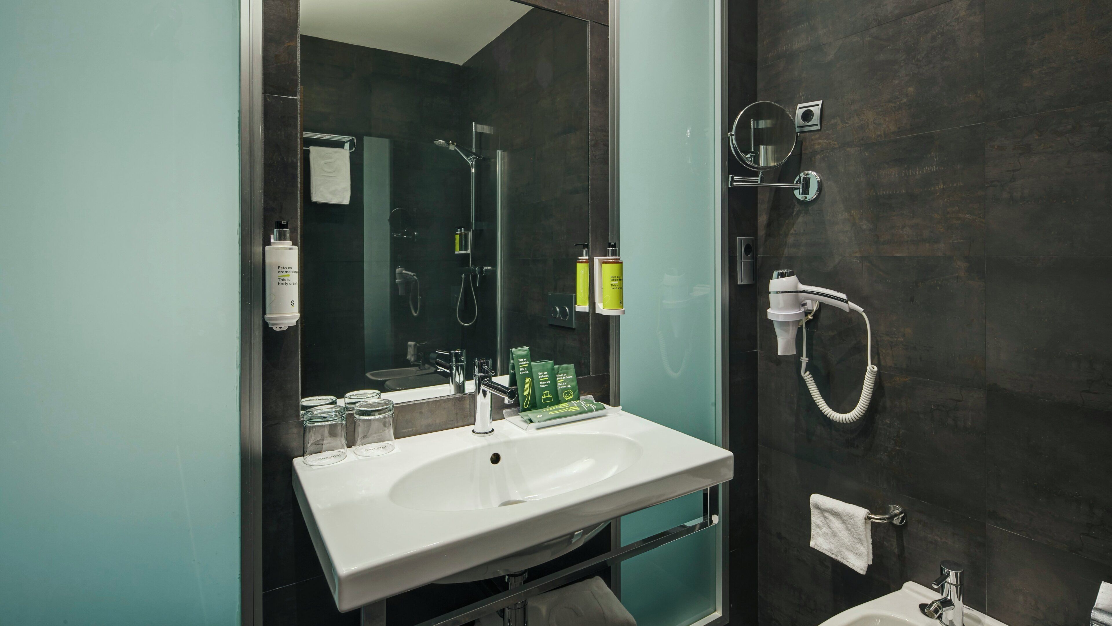 A modern bathroom with a white sink, a glass shower enclosure, and toiletries on the wall.
