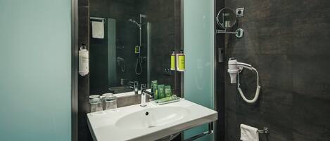 A modern bathroom with a white sink, a glass shower enclosure, and toiletries on the wall.